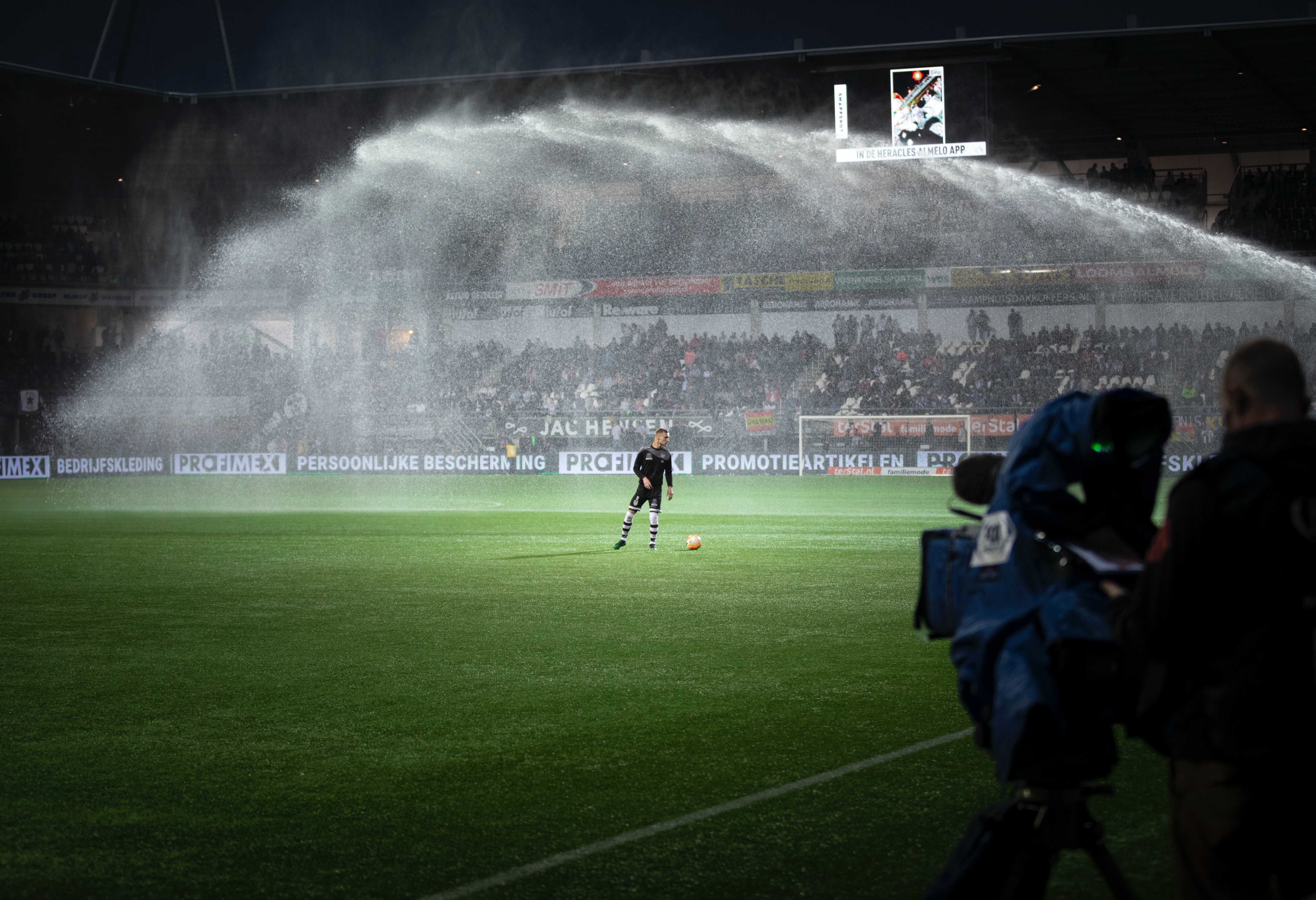 Football player on a pitch with water spraying over the top